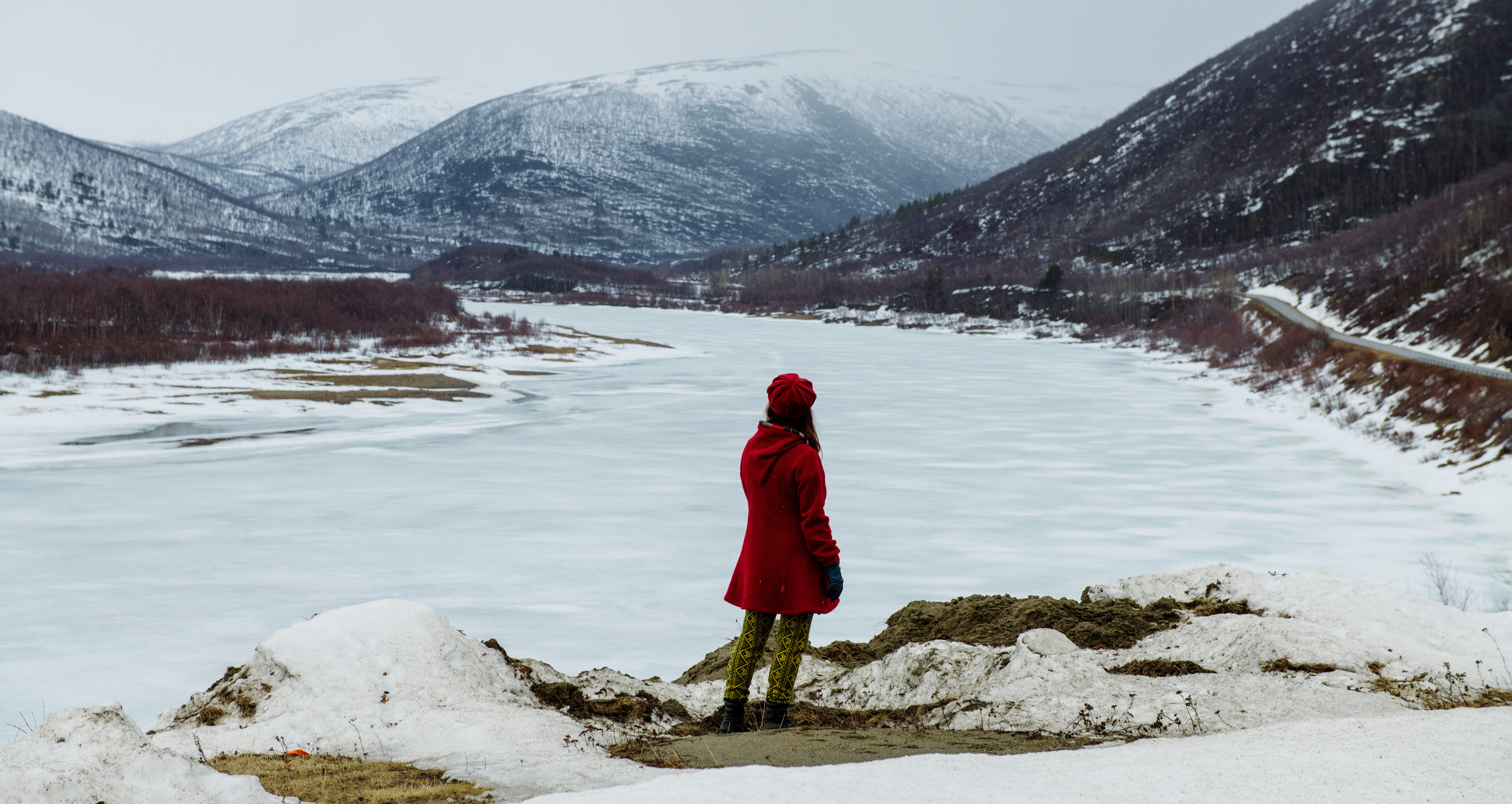 Practice-led design research professor, Maarit Mäkelä, looking into the horizon in front of a frozen lake and snowy mountains of Lapland.