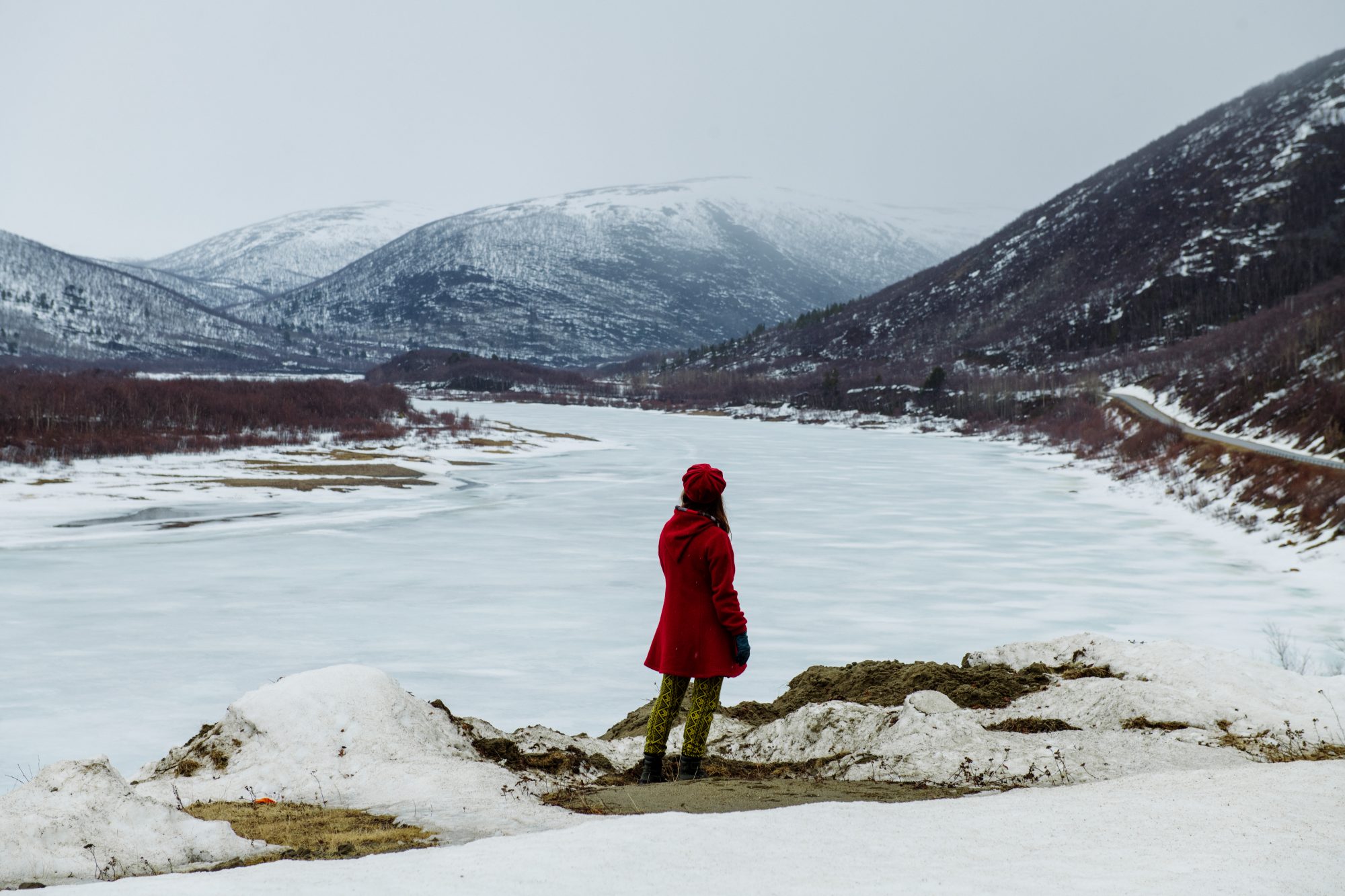 Practice-led design research professor, Maarit Mäkelä, looking into the horizon in front of a frozen lake and snowy mountains of Lapland.
